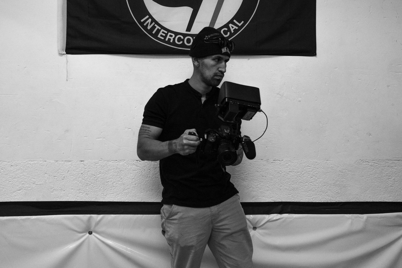 Camarógrafo con cámara de cine apoyado contra una pared, blanco y negro
